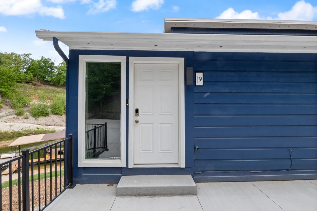 This image highlights the welcoming blue exterior wall of the condo, with a prominent front door and a large window. The scene suggests a peaceful and inviting entrance, ideal for couples seeking privacy and a calm start to their getaway. The porch hints at outdoor relaxation and the promise of tranquil mornings by the lake.
