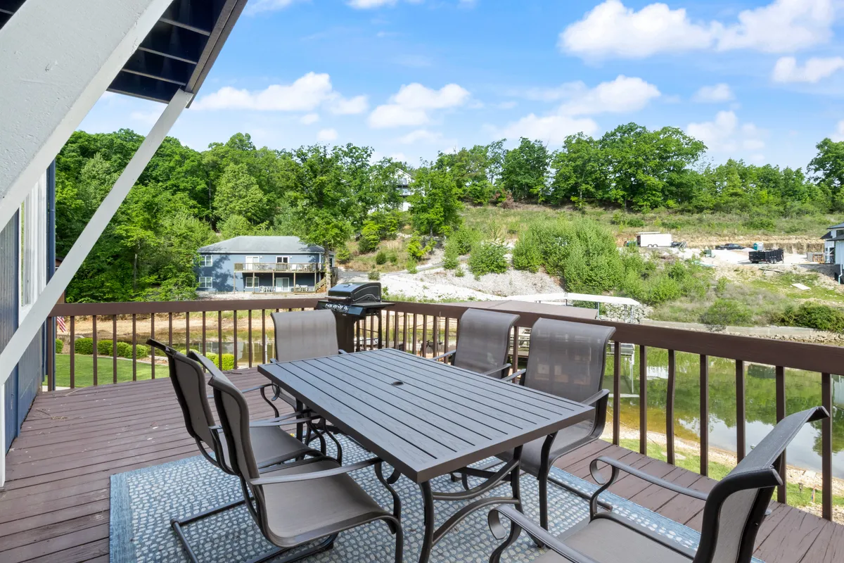 An exterior shot highlighting a cheerful outdoor dining area with a barbecue grill, surrounded by greenery and offering views of the water. The ambiance is friendly and relaxed, ideal for gatherings.