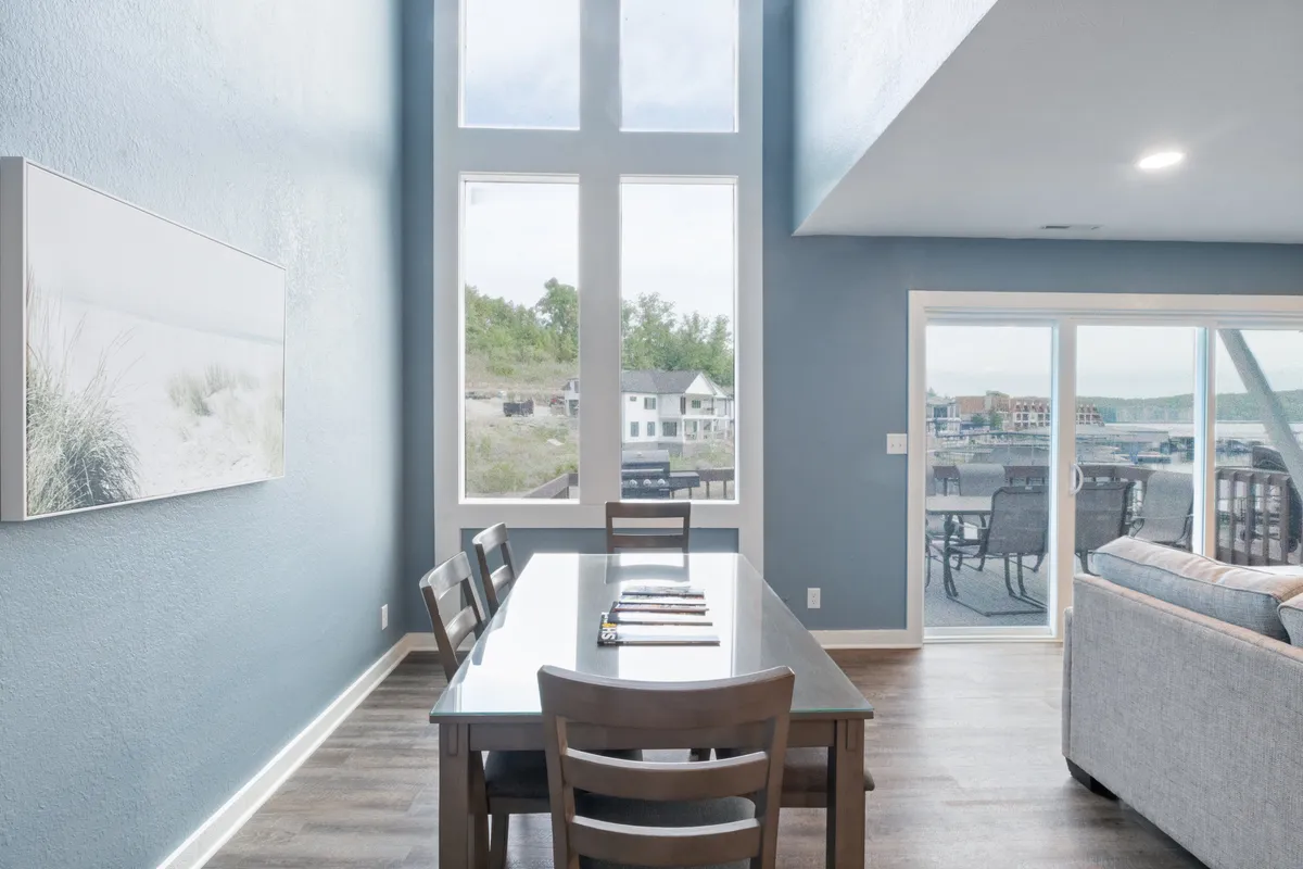 A stylish dining area with a large table and comfortable seating, set beside expansive windows that overlook the outdoors. Artistic touches on the wall and warm natural light create an inviting atmosphere perfect for meals, game nights, or simply enjoying the view.