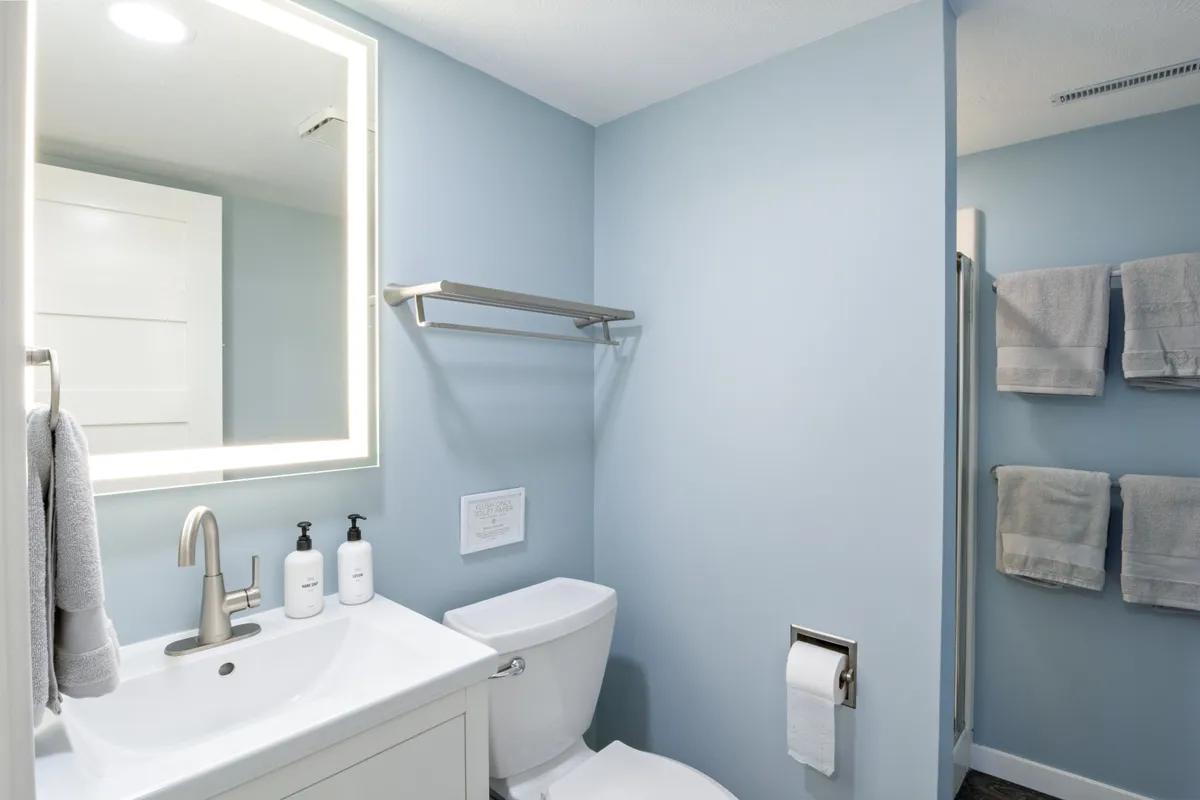 A fresh, modern bathroom with a well-lit vanity and sink, a spacious shower area, toilet, and neatly arranged towels. The space is bright and inviting, designed for comfort and convenience.