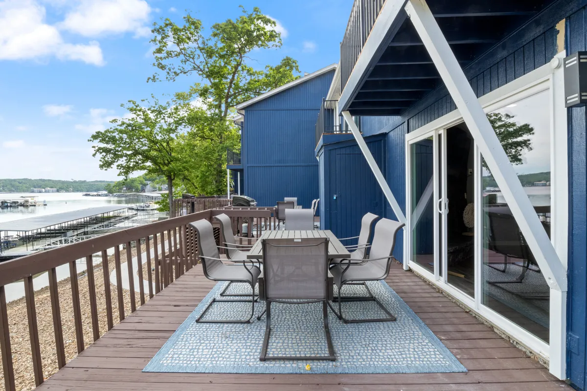 This exterior image features a lakeside deck area with an outdoor dining table and chairs, overlooking tranquil water and surrounded by natural greenery. The scene exudes relaxation and invites guests to unwind or share a meal with loved ones while enjoying scenic views of the cove.