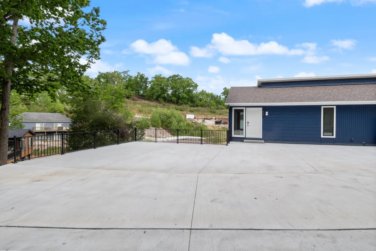 A modern house facade with a spacious concrete patio surrounded by greenery. The patio offers ample space for outdoor games, relaxation, and gatherings, set against a backdrop of nature.