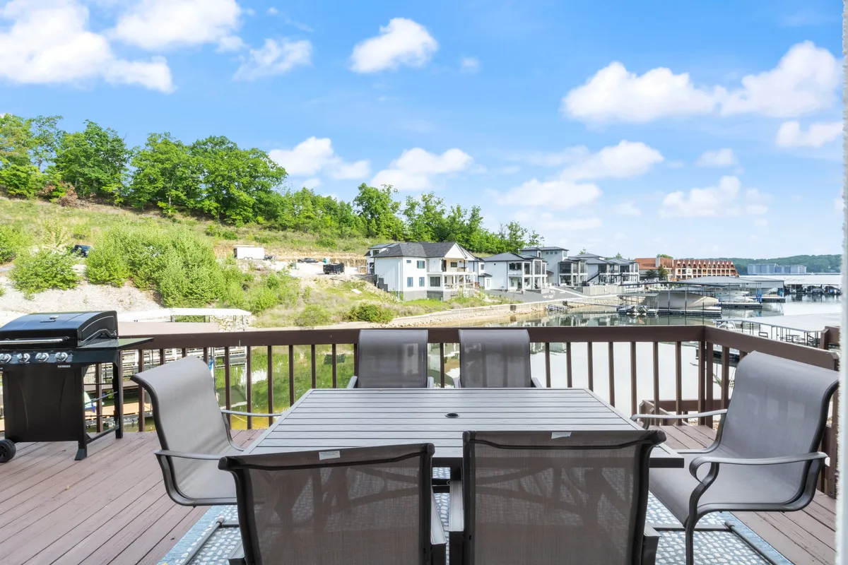 An inviting outdoor dining area with a large table and grill overlooking the serene lake. The view features lush greenery and calm waters, suggesting easy access to lakeside relaxation and group gatherings.