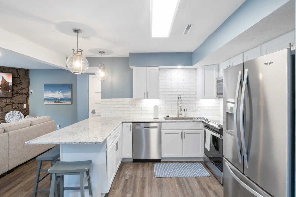 A warm, welcoming kitchen with a large island, stainless steel appliances, pendant lighting, and a striking stone wall feature. The setup encourages group meal preparation and casual get-togethers, embodying the spirit of shared experiences.