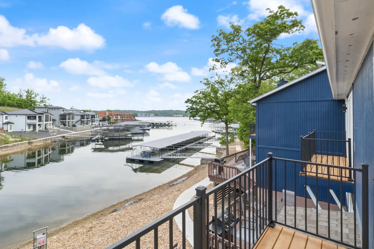 A tranquil waterfront view featuring docked boats, lush greenery, and the modern architecture of the lakeside home. The setting is serene, with ample opportunity for boating, fishing, or simply enjoying the scenery.