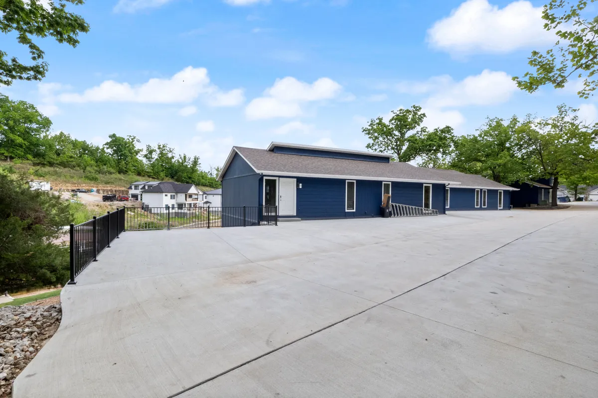 An inviting exterior shot of the modern blue house with a spacious concrete patio and lush greenery surrounding the property. The open space is ideal for outdoor gatherings, barbecues, or playful moments with pets.