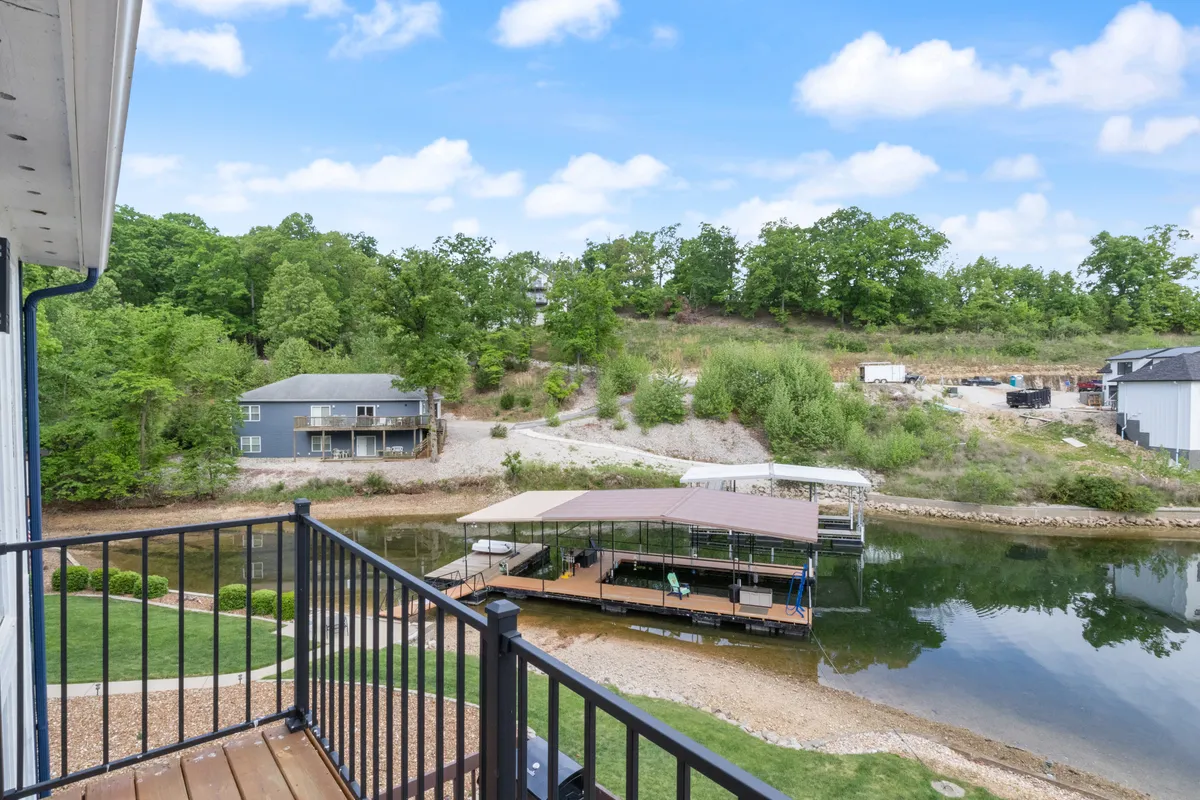 A wide view of the lake, boat dock, and houses nestled in greenery, with ample space for swimming, fishing, or simply taking in the peaceful sunset. The gentle water and minimal waves suggest safety and tranquility.